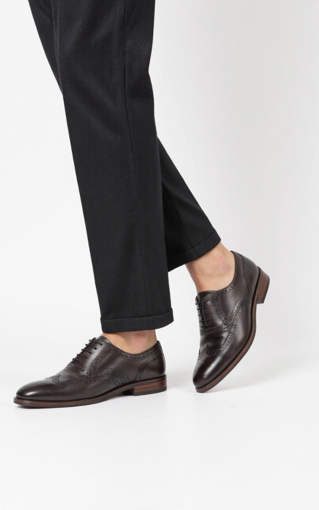 A male model wearing Brogue shoes, against a white background, with a close   up of the feet